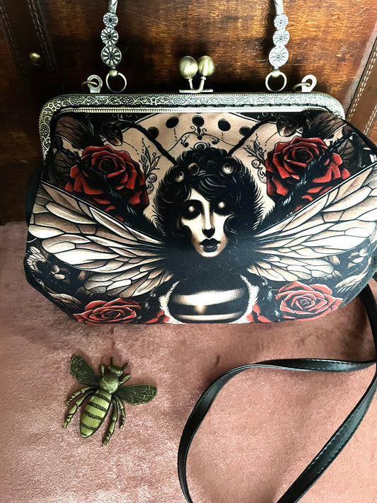 Sac à main rétro avec illustration femme-papillon et roses rouges, fermoir métallique effet bronze.