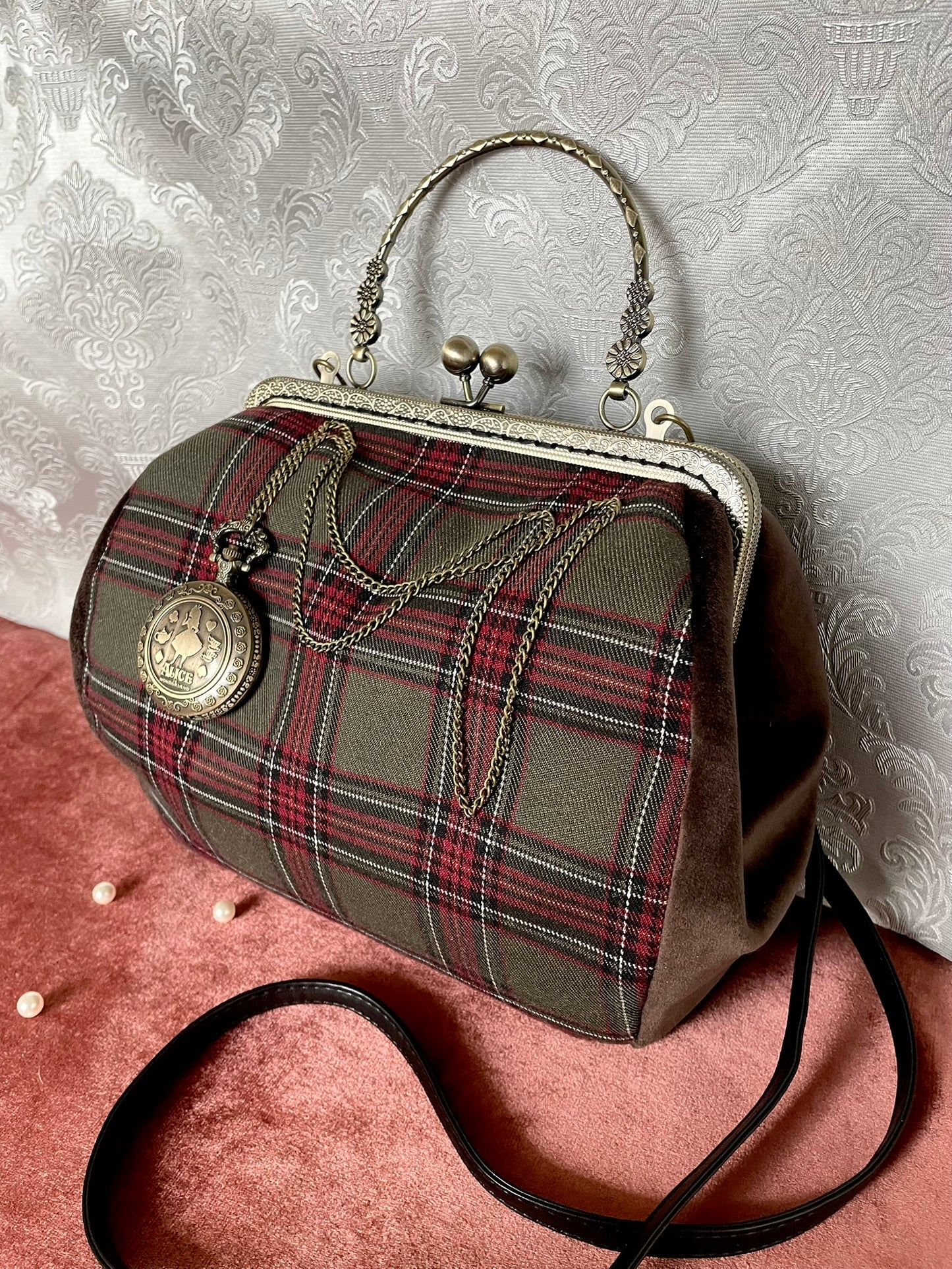 Sac à main tartan porté épaule avec bandoulière noire et poignée rigide ciselée.