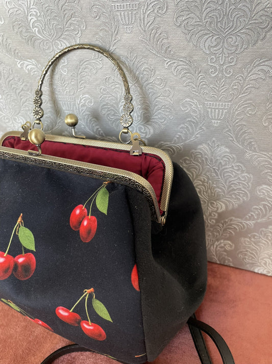 Vue de trois-quarts sac retro velours noir motif cerises rouges et fermoir bronze