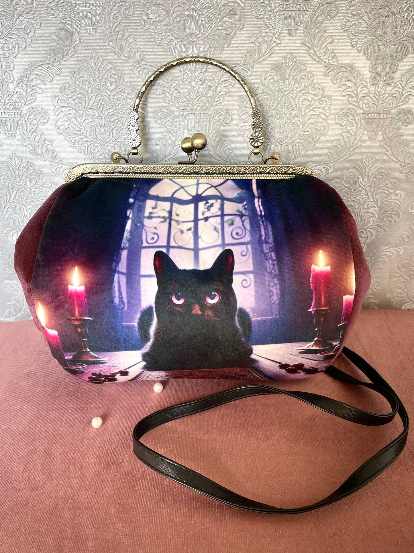 Détail de profil d'un sac à main rétro en velours lie de vin illustrant un chat noir éclairé par des bougies dans une ambiance gothique.