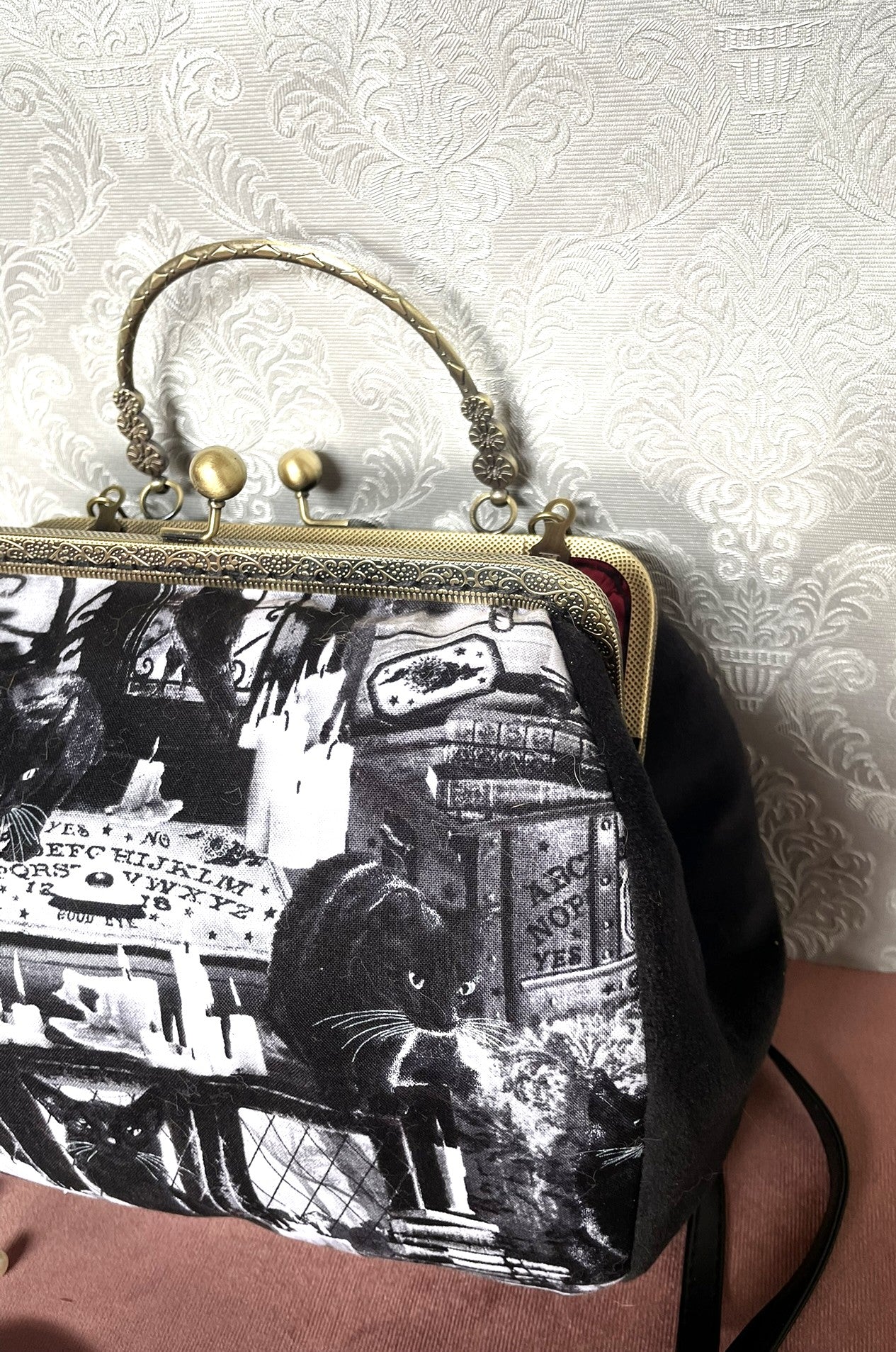 Vue de profil d'un sac rétro en velours noir à motif mystique de chats noirs et grimoires.