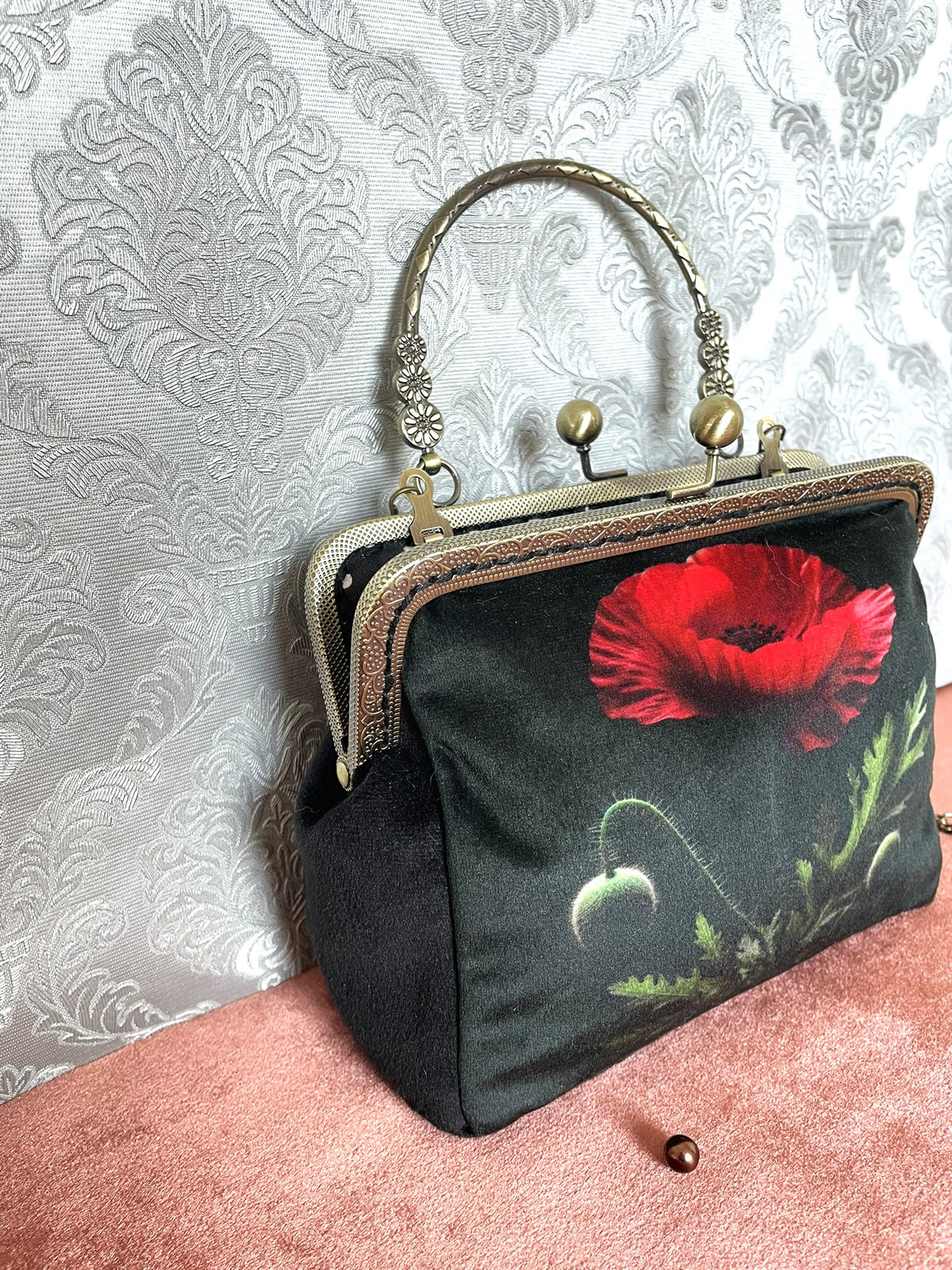 Gros plan velours noir et fermoir bronze cisele d'un sac retro coquelicot