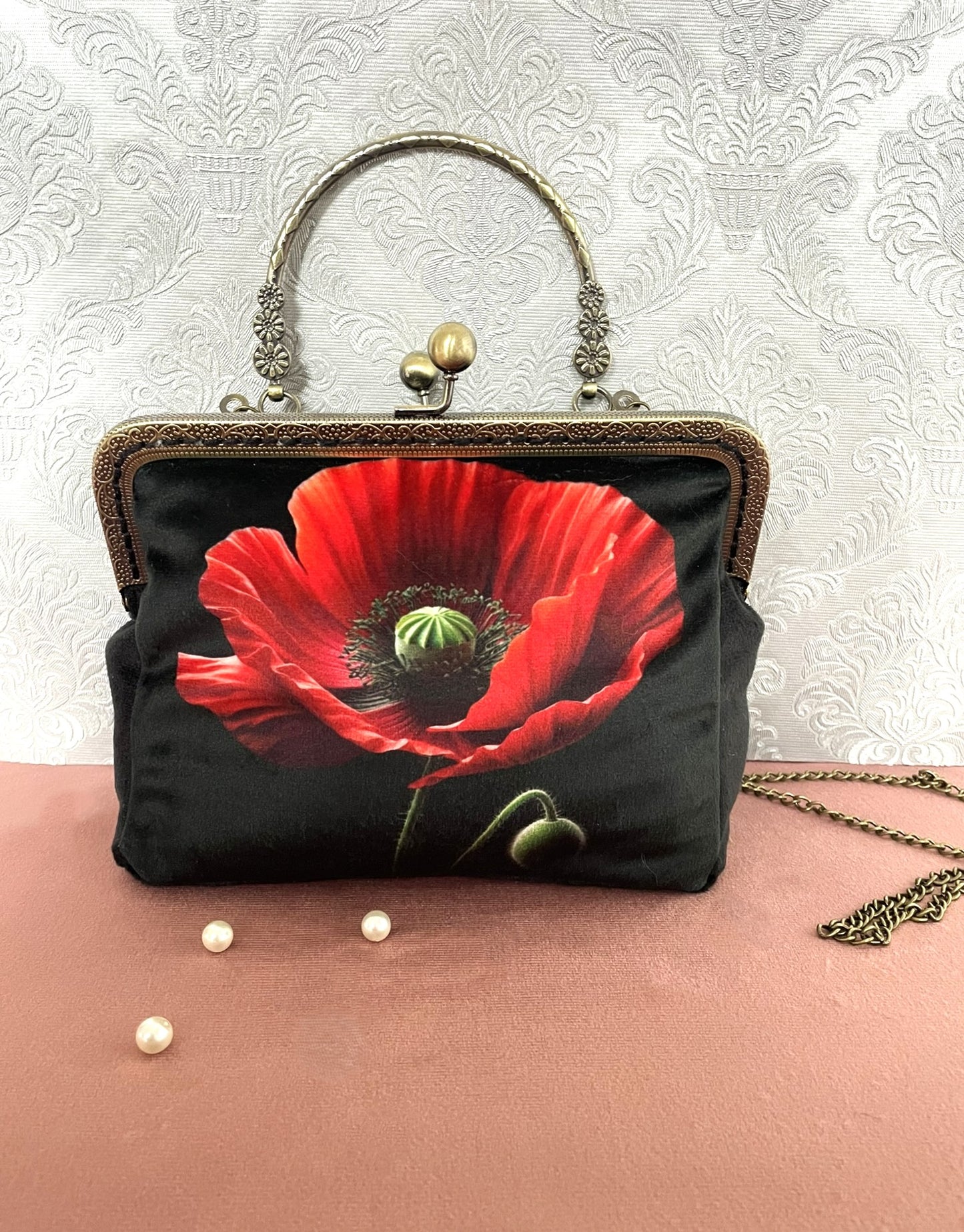 Sac pochette rétro de face en velours noir avec illustration d'un grand coquelicot rouge vif, poignée rigide ciselée et chaîne en métal.