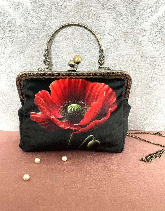 Sac pochette rétro de face en velours noir avec illustration d'un grand coquelicot rouge vif, poignée rigide ciselée et chaîne en métal.
