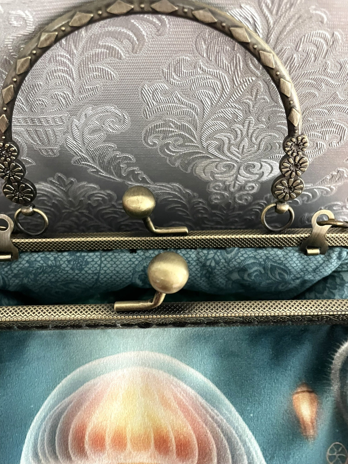 Gros plan fermoir effet bronze ciselé et doublure coton bleu canard motif dentelle d'un sac retro méduse