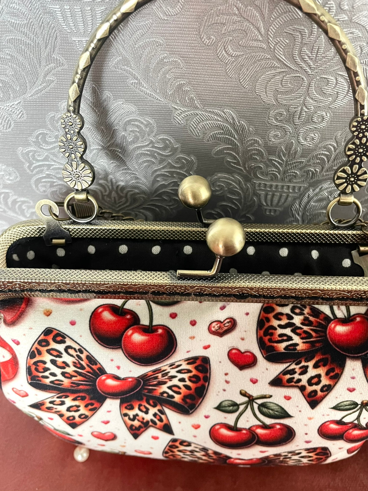 Gros plan fermoir effet bronze cisele et doublure coton noir a pois blancs d'un sac retro cerises