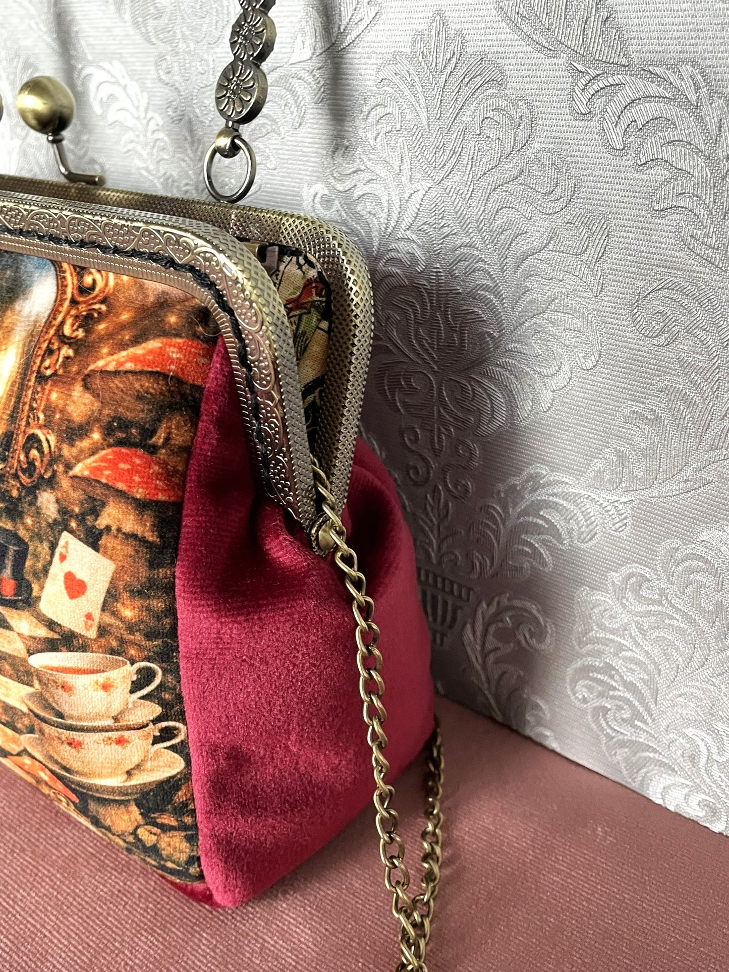 Gros plan latéral d'une pochette clutch féerique en velours bordeaux avec motif imprimé Alice au Pays des Merveilles et chaîne.