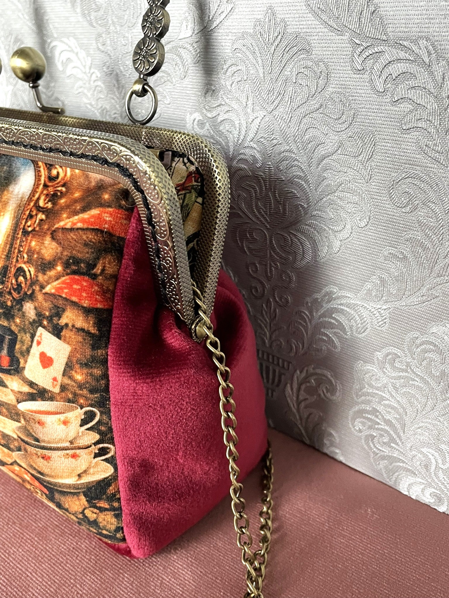 Gros plan latéral d'une pochette clutch féerique en velours bordeaux avec motif imprimé Alice au Pays des Merveilles et chaîne.