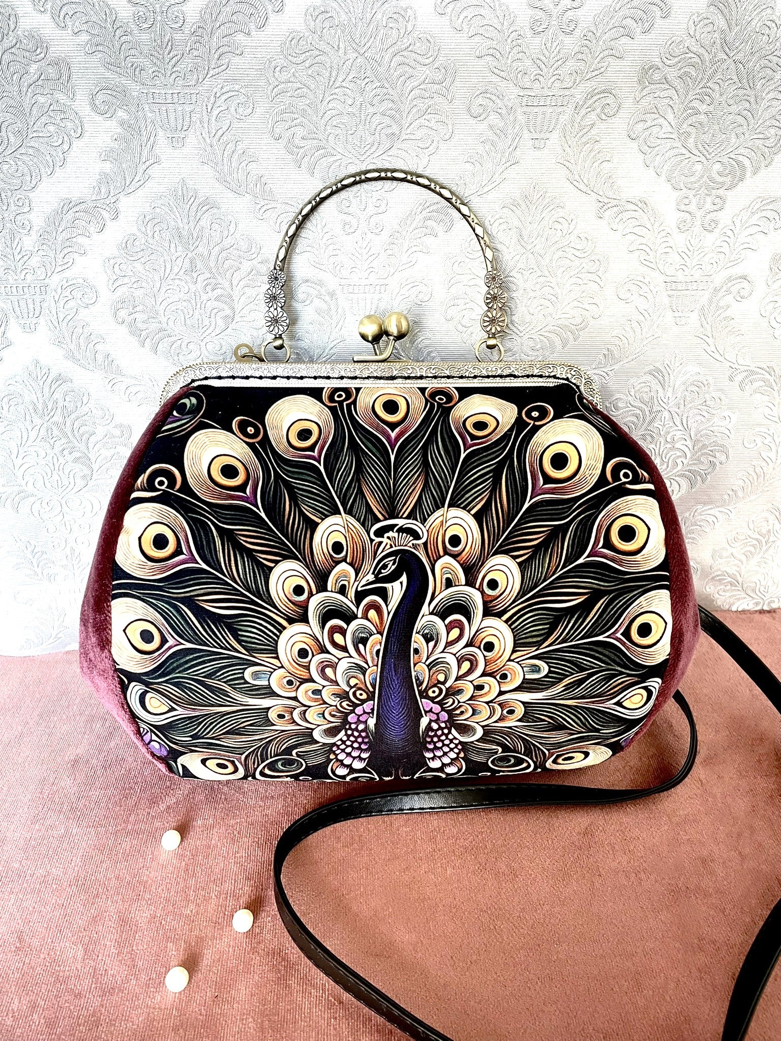 Détail de profil d'un sac à main rétro en velours lie de vin illustrant les plumes d'un paon royal avec fermoir bronze antique.