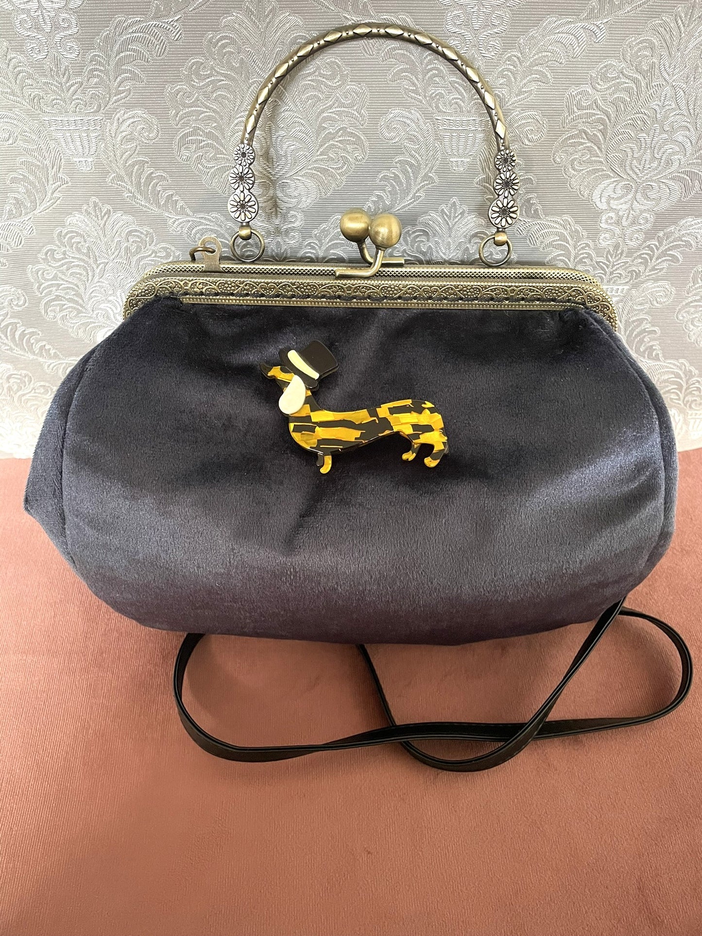 Détail de profil d'un sac à main rétro en velours bleu nuit orné d'une broche teckel en résine et haut-de-forme.