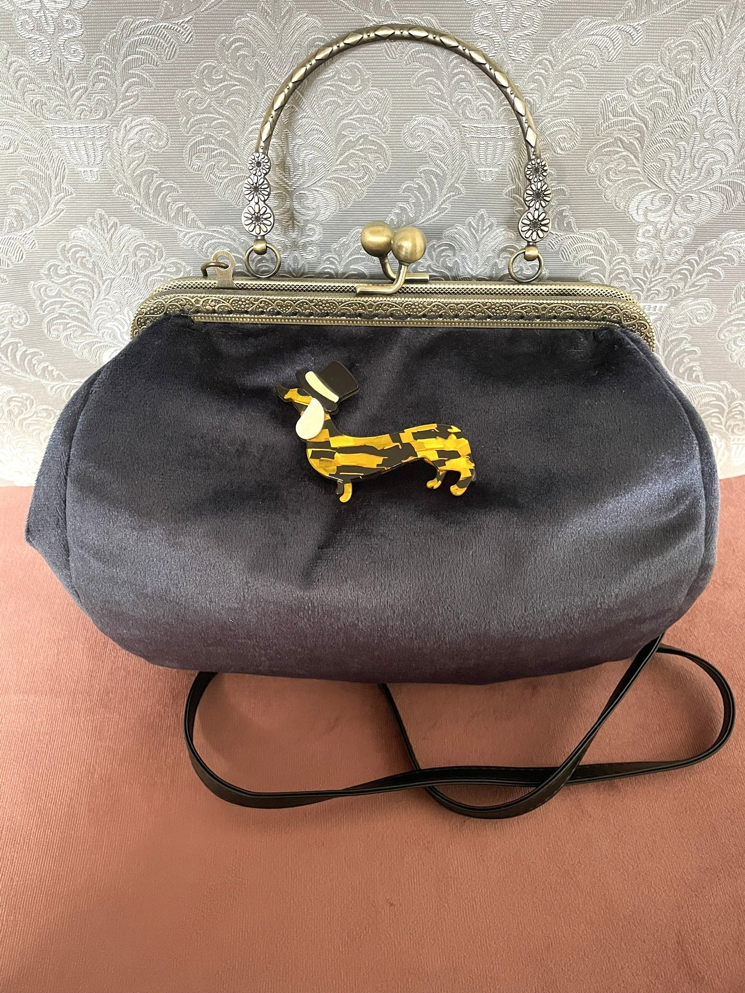 Détail de profil d'un sac à main rétro en velours bleu nuit orné d'une broche teckel en résine et haut-de-forme.