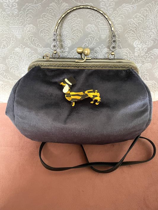 Détail de profil d'un sac à main rétro en velours bleu nuit orné d'une broche teckel en résine et haut-de-forme.