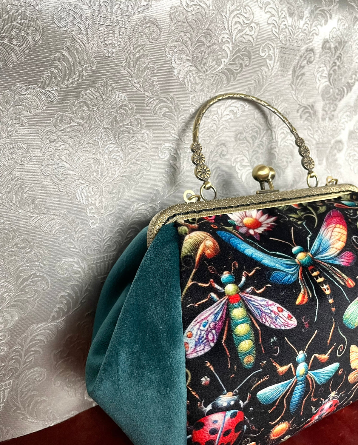 Vue de côté d'un sac rétro à fermoir vintage en velours vert canard avec imprimé insectes multicolores