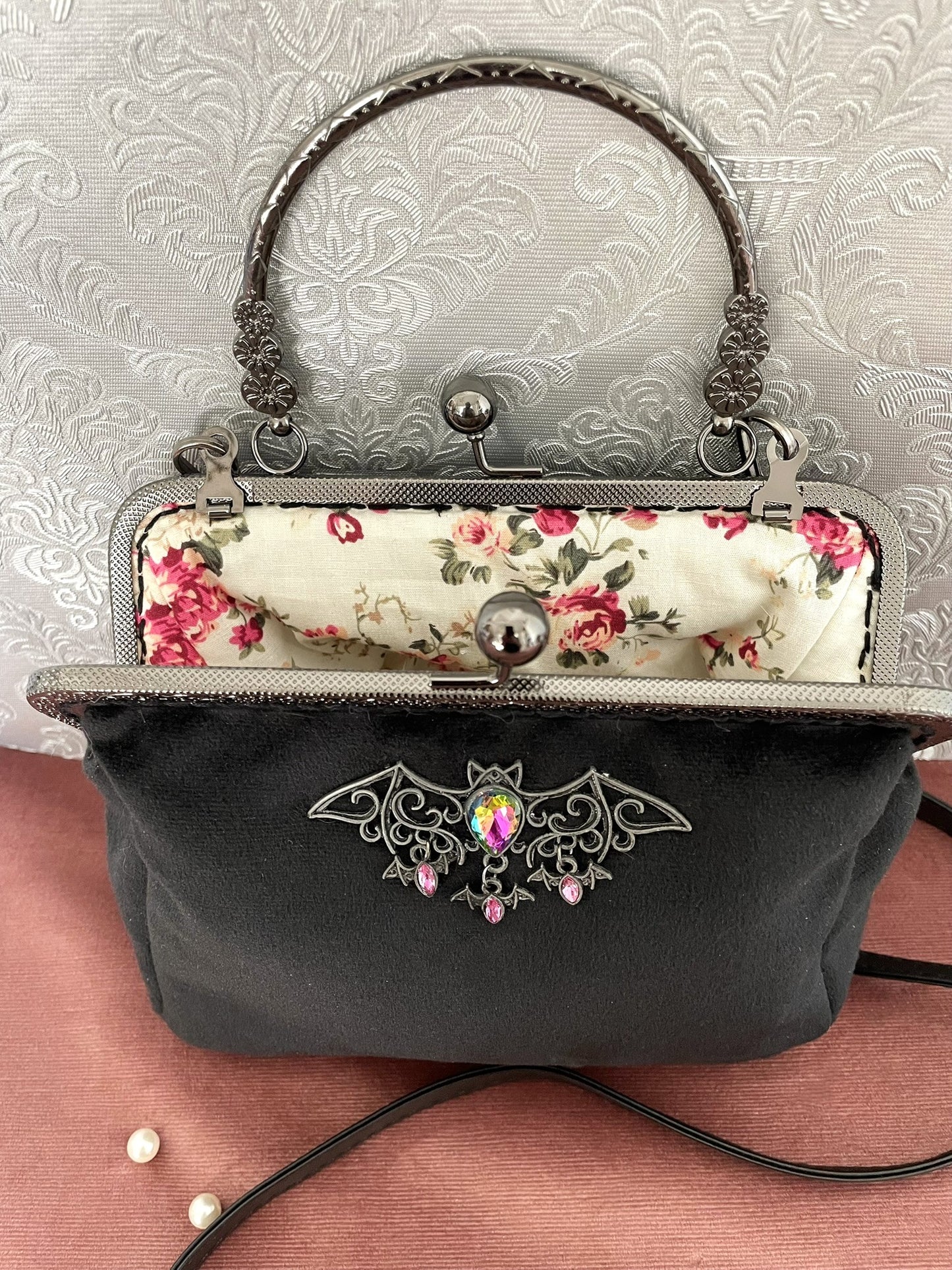 Sac rétro ouvert en velours noir révélant sa doublure fleurie à roses anciennes et son fermoir clic-clac gunmetal orné d'un bijou chauve-souris - Le Comptoir de Suzanne