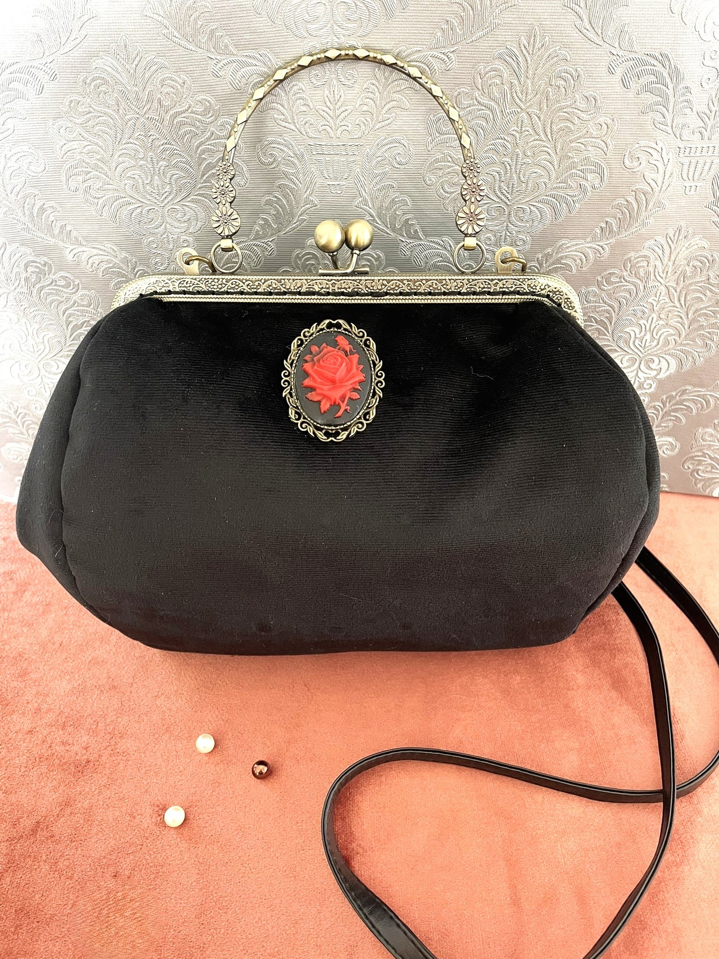 Gros plan sur le camée rose rouge et la poignée ciselée du sac vintage noir.