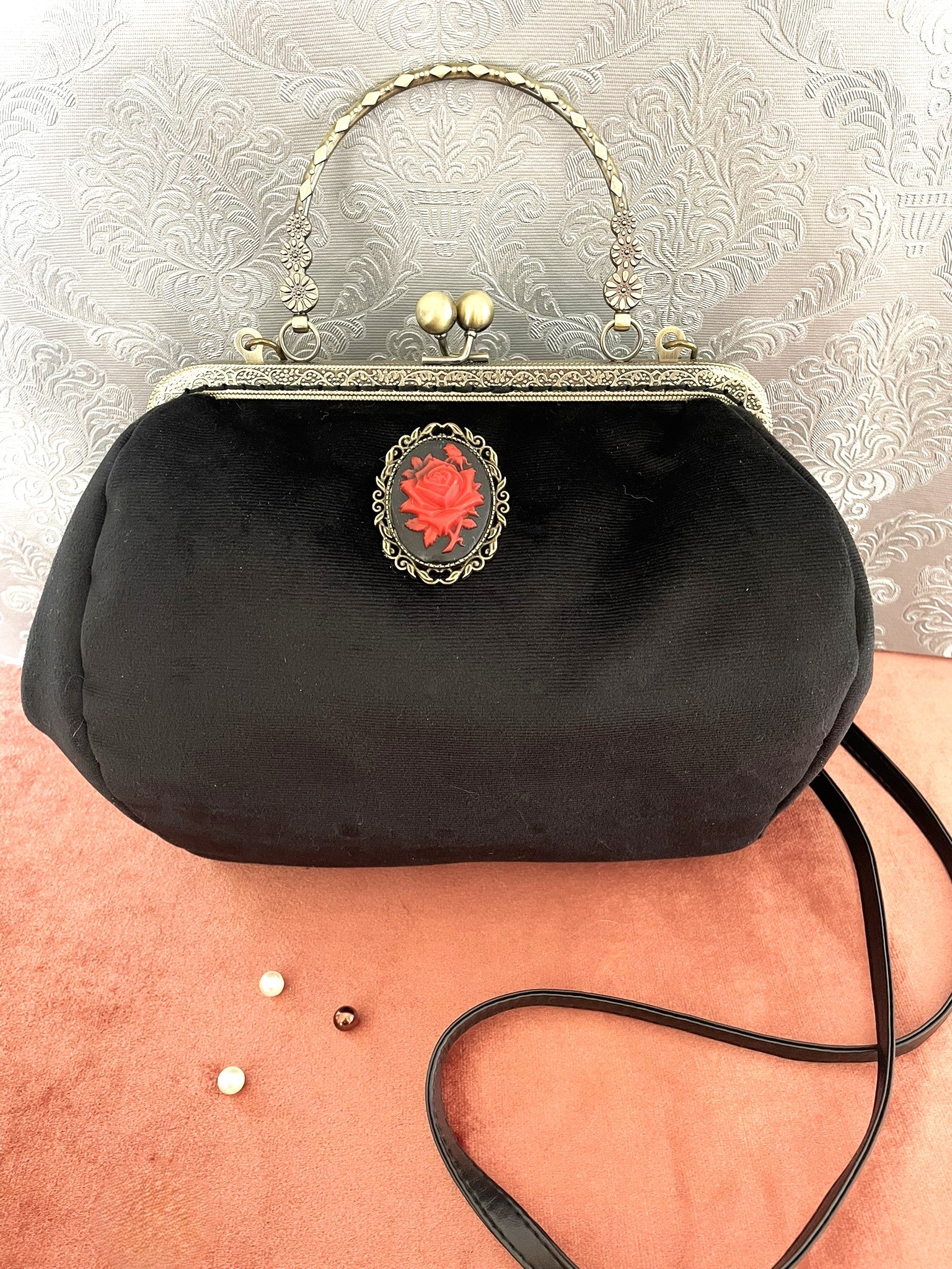 Gros plan sur le camée rose rouge et la poignée ciselée du sac vintage noir.